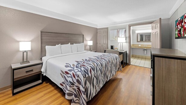 A hotel room with a bed, bedside tables, a desk, a mirror, and a bathroom visible through an open door. - Red Roof Inn Ardmore (Ardmore)