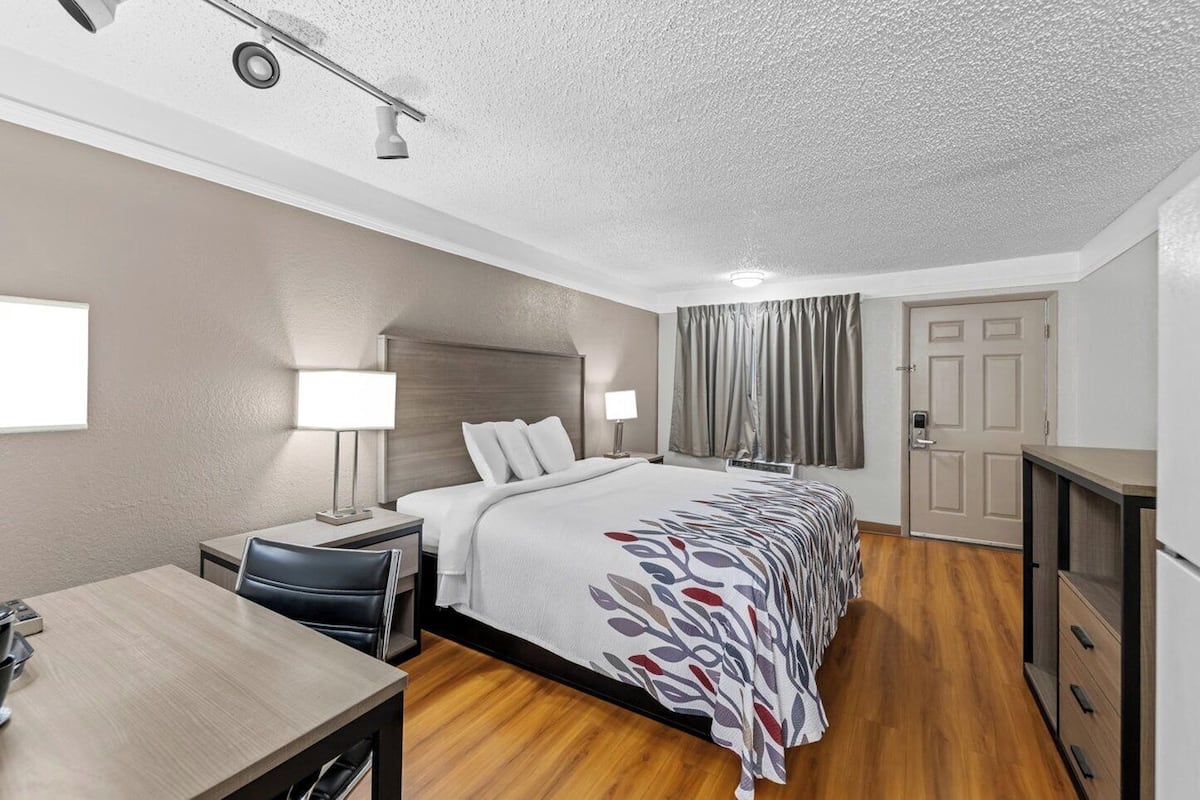A hotel room with a bed, bedside tables, a desk, a chair, a wardrobe, a door, and a window.