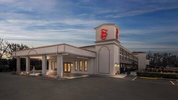 A Red Roof Inn with a covered parking area, a fountain, and a clear sky.