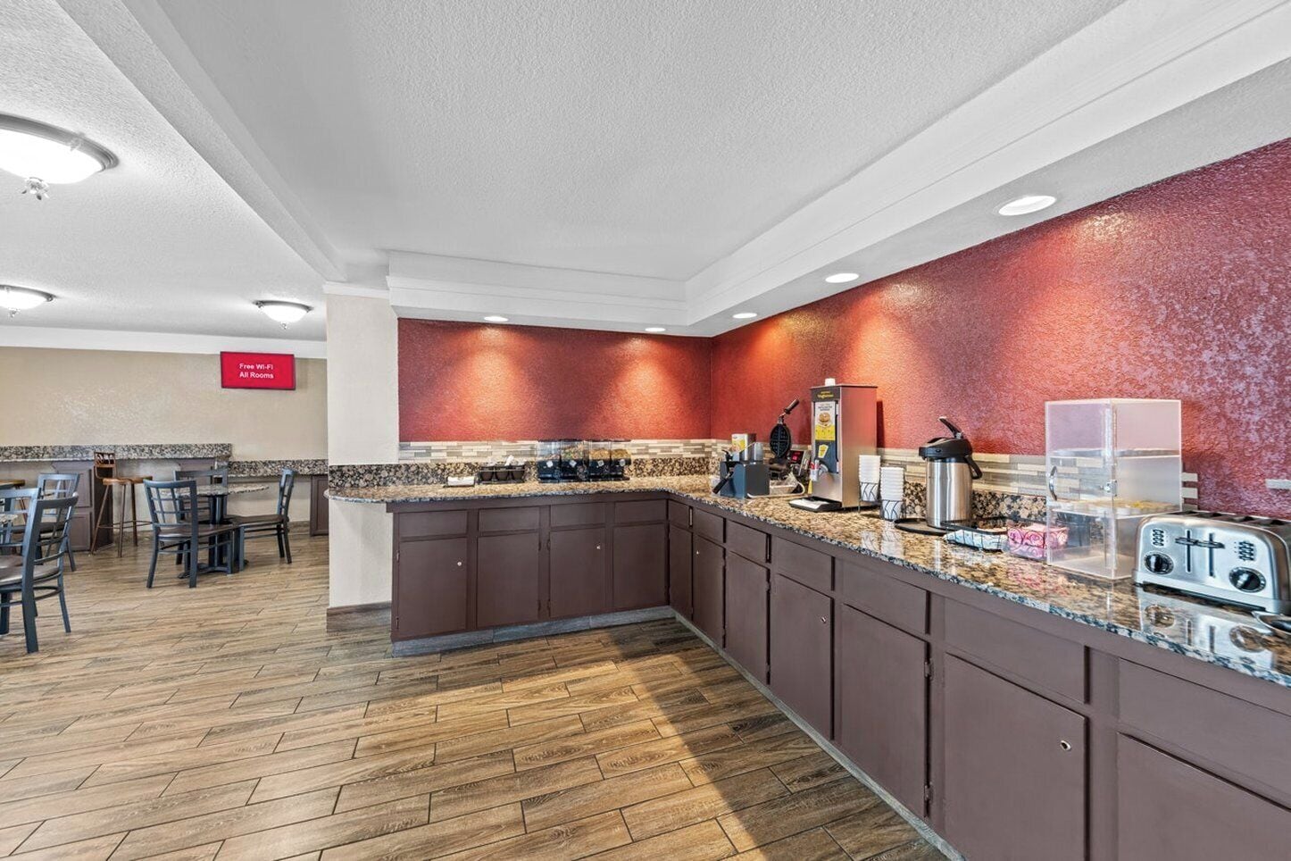 Una cocina de hotel con encimera de granito, electrodomésticos de acero inoxidable y pared texturizada de color rojo.