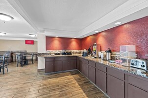 Una cocina de hotel con encimera de granito, electrodomésticos de acero inoxidable y pared texturizada de color rojo.
