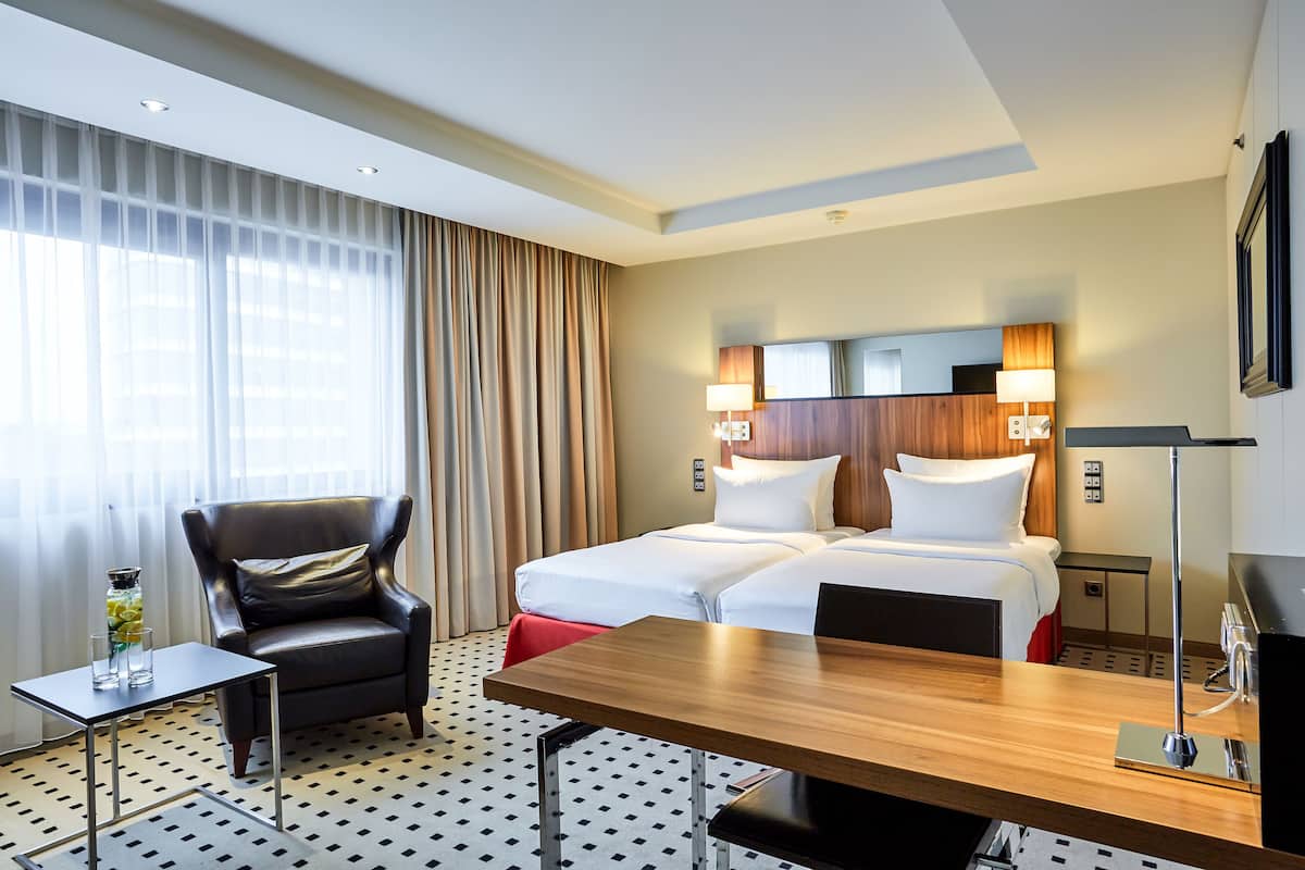 A hotel room with a bed, a chair, a table, and a lamp.