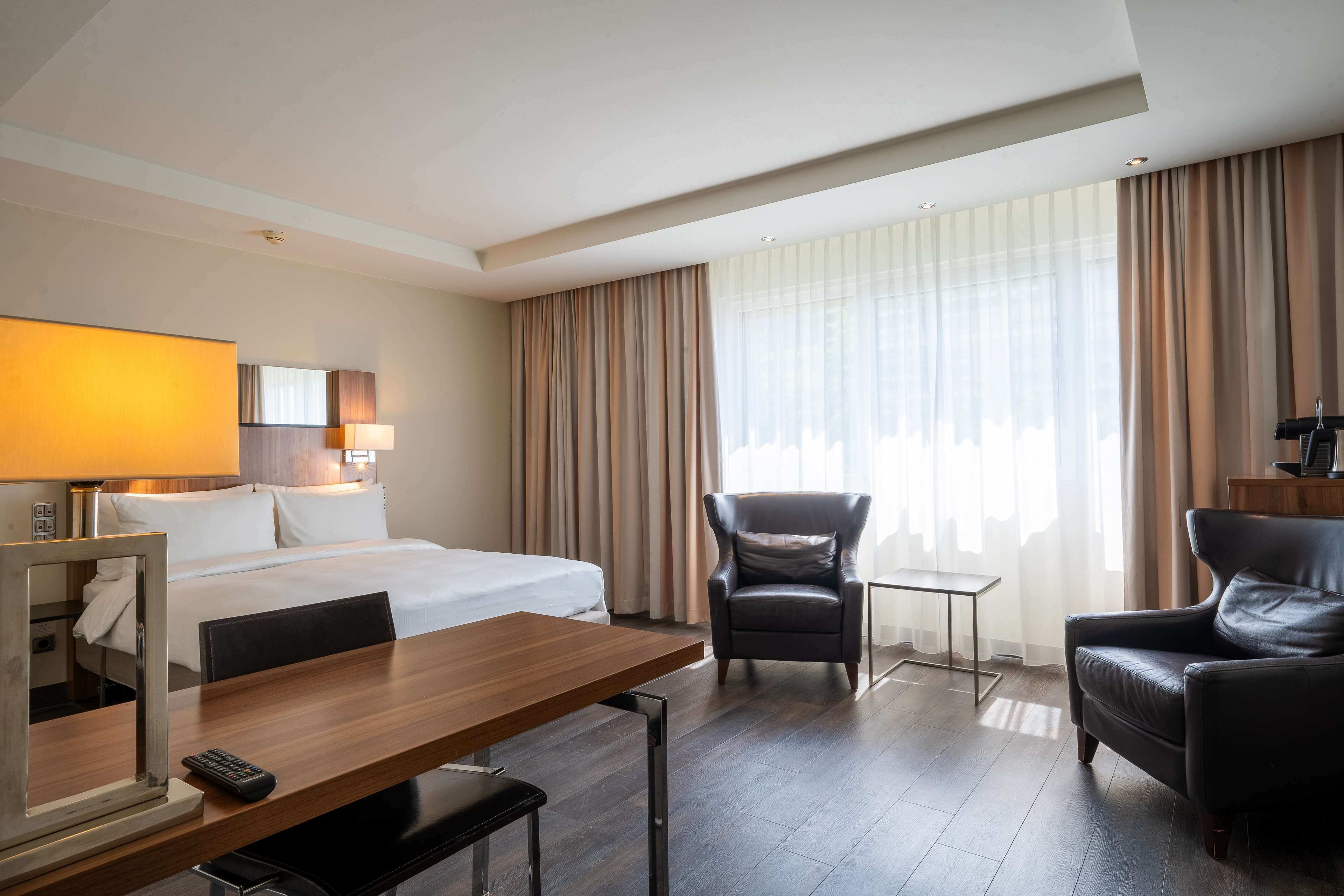 Een hotelkamer met een bed, een bureau, een stoel, een klein tafeltje en een lamp.