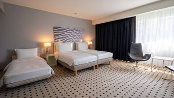 A hotel room with two beds, a desk, a chair, and a large window with curtains.