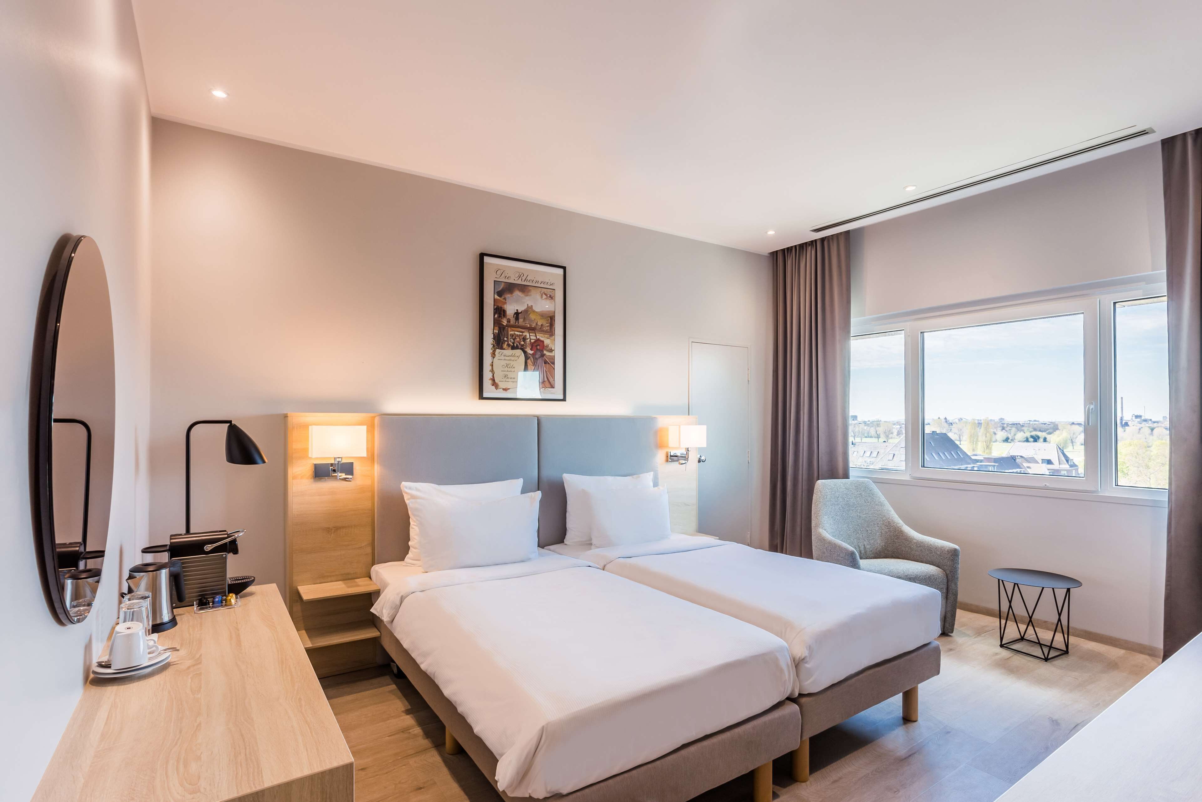 Ein Hotelzimmer mit zwei Betten, einem Schreibtisch mit Lampe, einem Sessel und einem Fenster mit Aussicht.