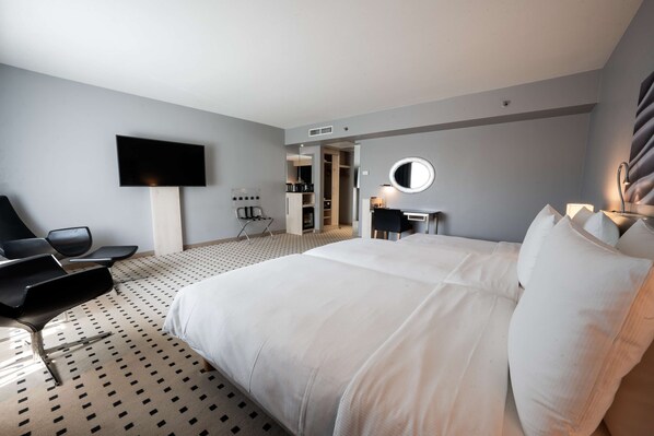 A hotel room with a large bed, a flat-screen TV mounted on the wall, a desk with a chair, and a walk-in closet.