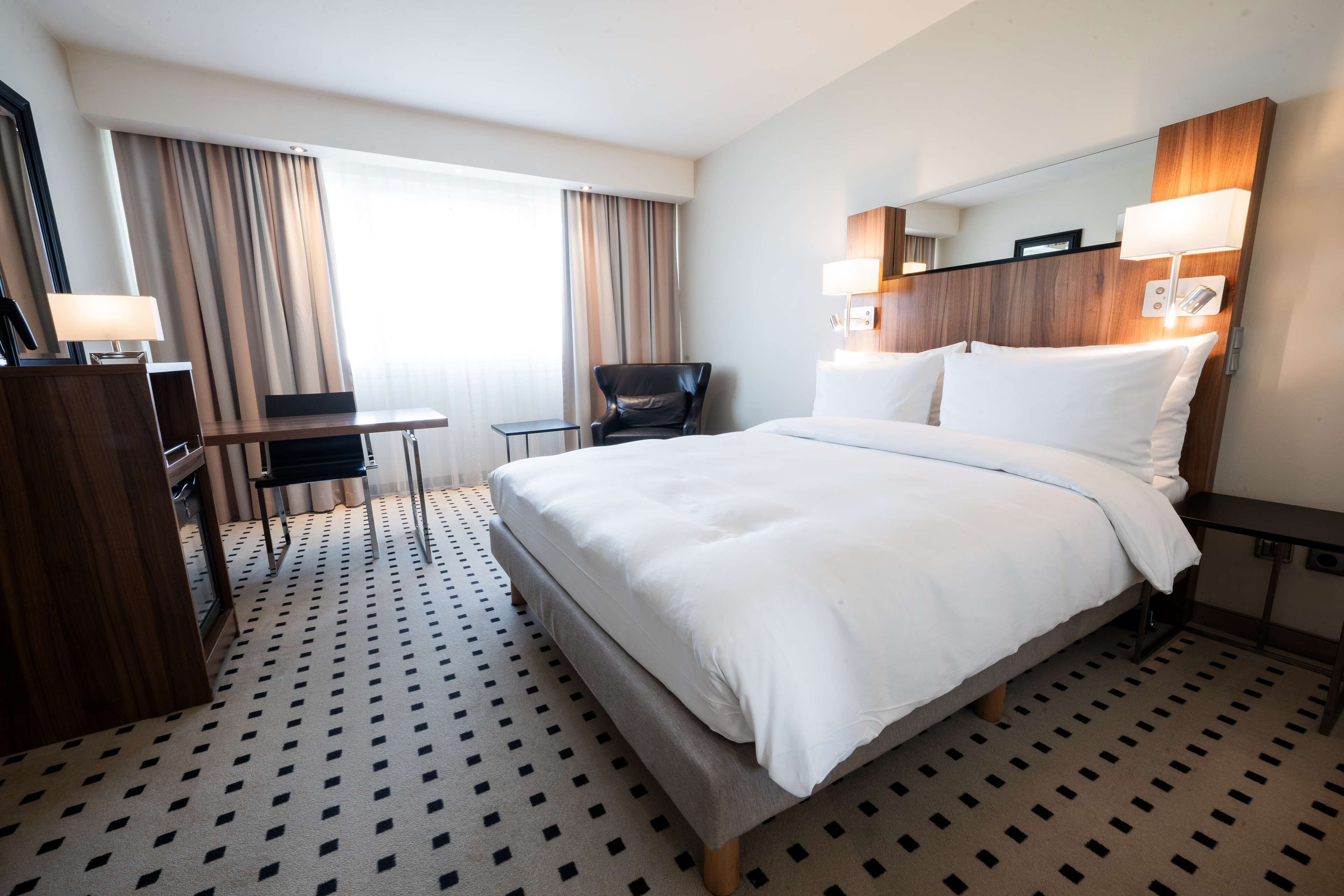 Et hotelværelse med en stor seng, et skrivebord, en stol og et spejl.