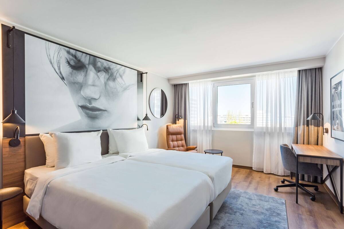 A hotel room with a large bed, a desk, a chair, and a window with curtains.