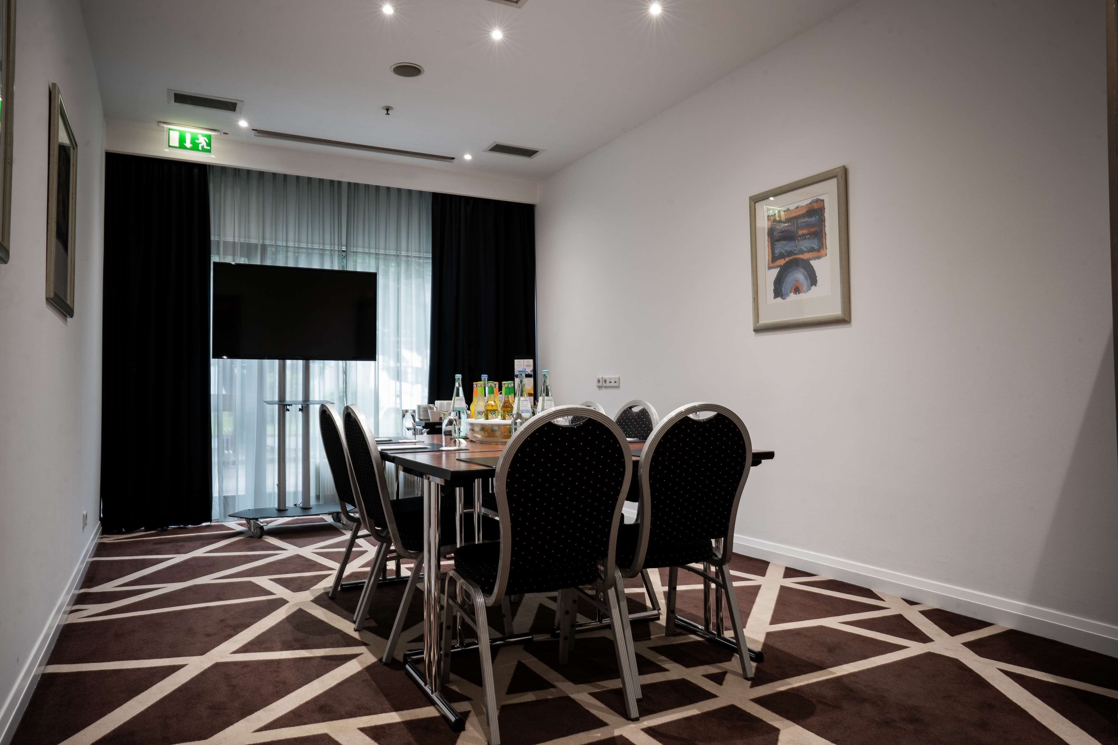 A conference room with a round table, six chairs, a projector screen, and a painting on the wall.