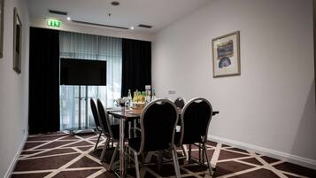 A conference room with a round table, six chairs, a projector screen, and a painting on the wall.