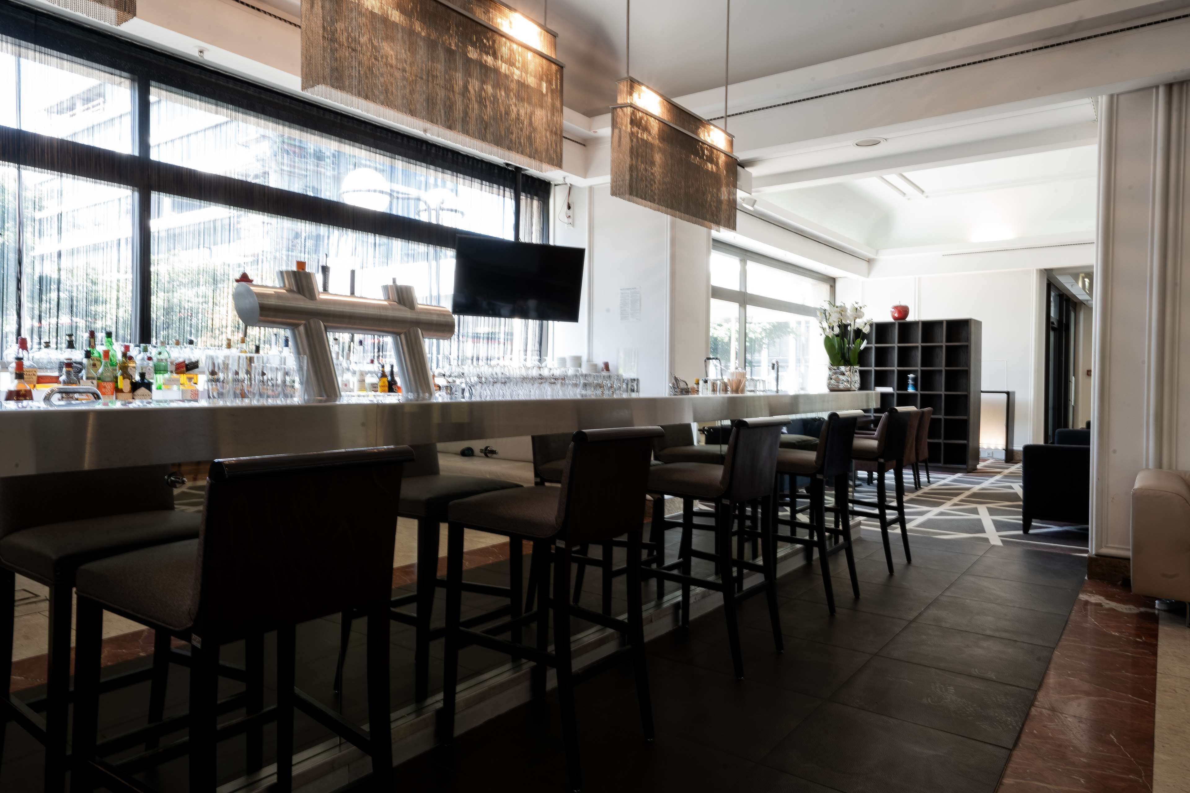 Eine moderne Bar mit einer langen Theke, mehreren Barhocker und einem Fernsehbildschirm.