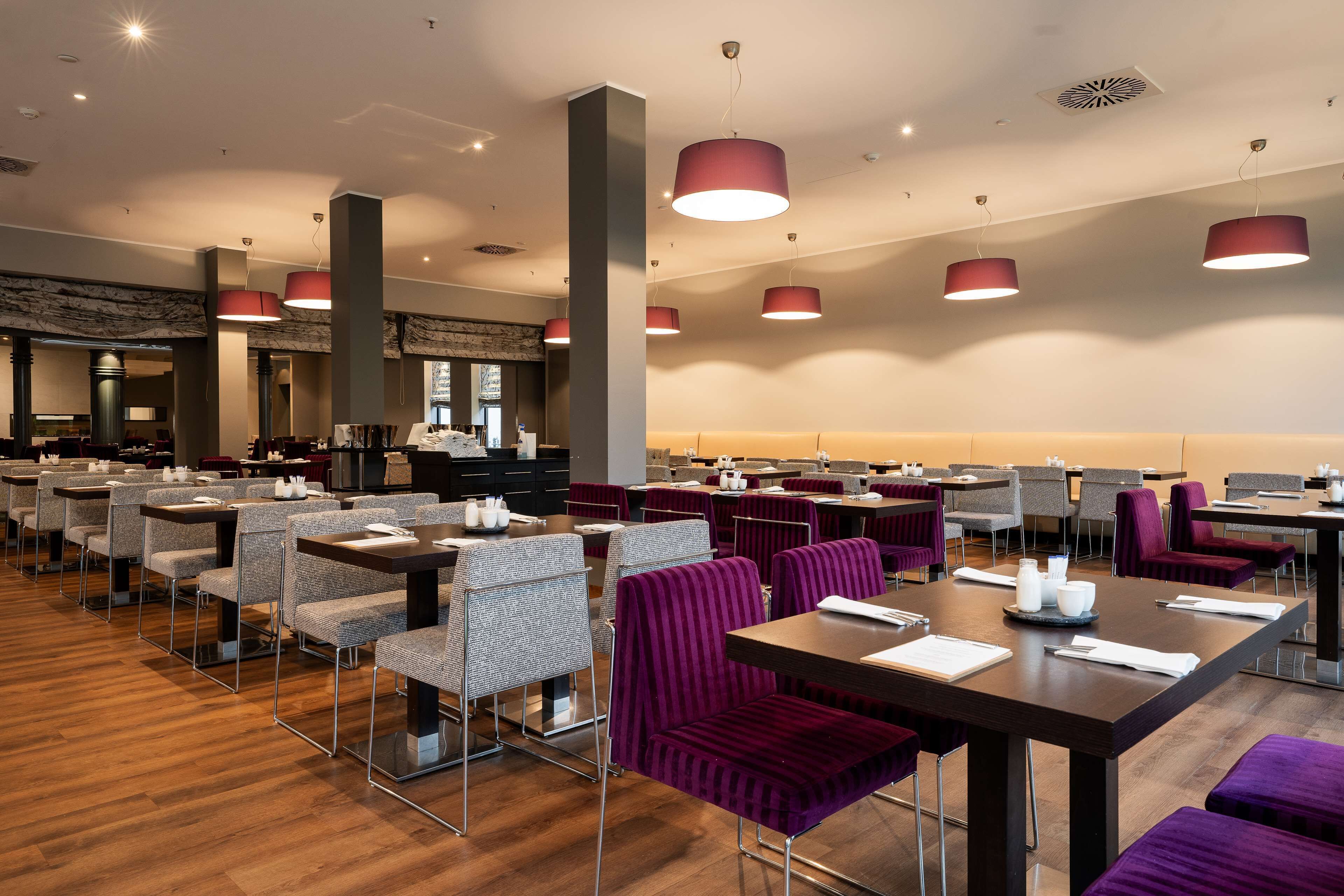 A modern dining area with multiple tables and chairs, some with purple upholstery.