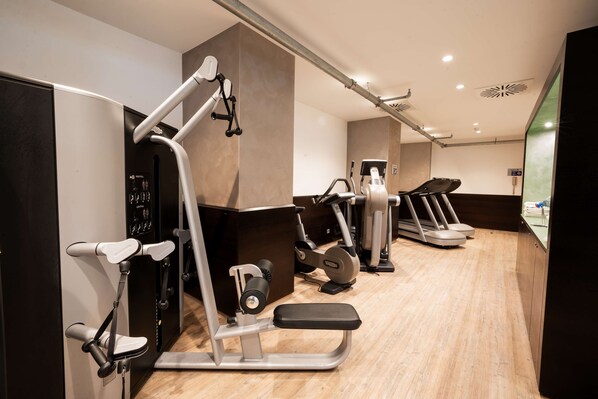 Un gimnasio moderno con diversas máquinas de ejercicio, incluyendo cintas de correr y estaciones de pesas, dispuesto en un espacio amplio.