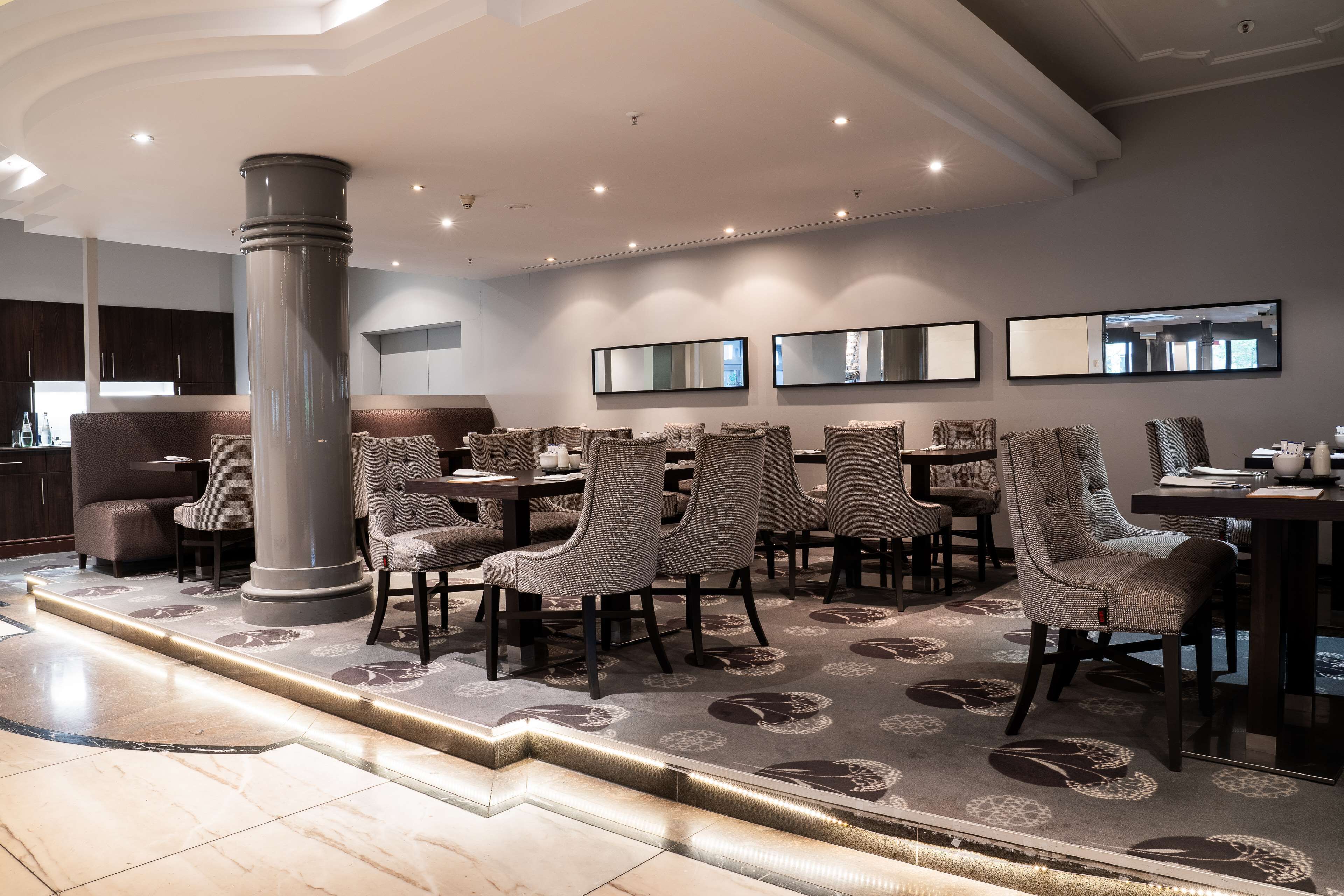 A modern dining area with a central column, multiple tables, and chairs.