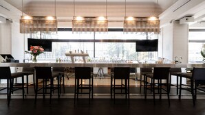 A modern bar area with a long counter, multiple bar stools, and a large window providing a view of the outside.