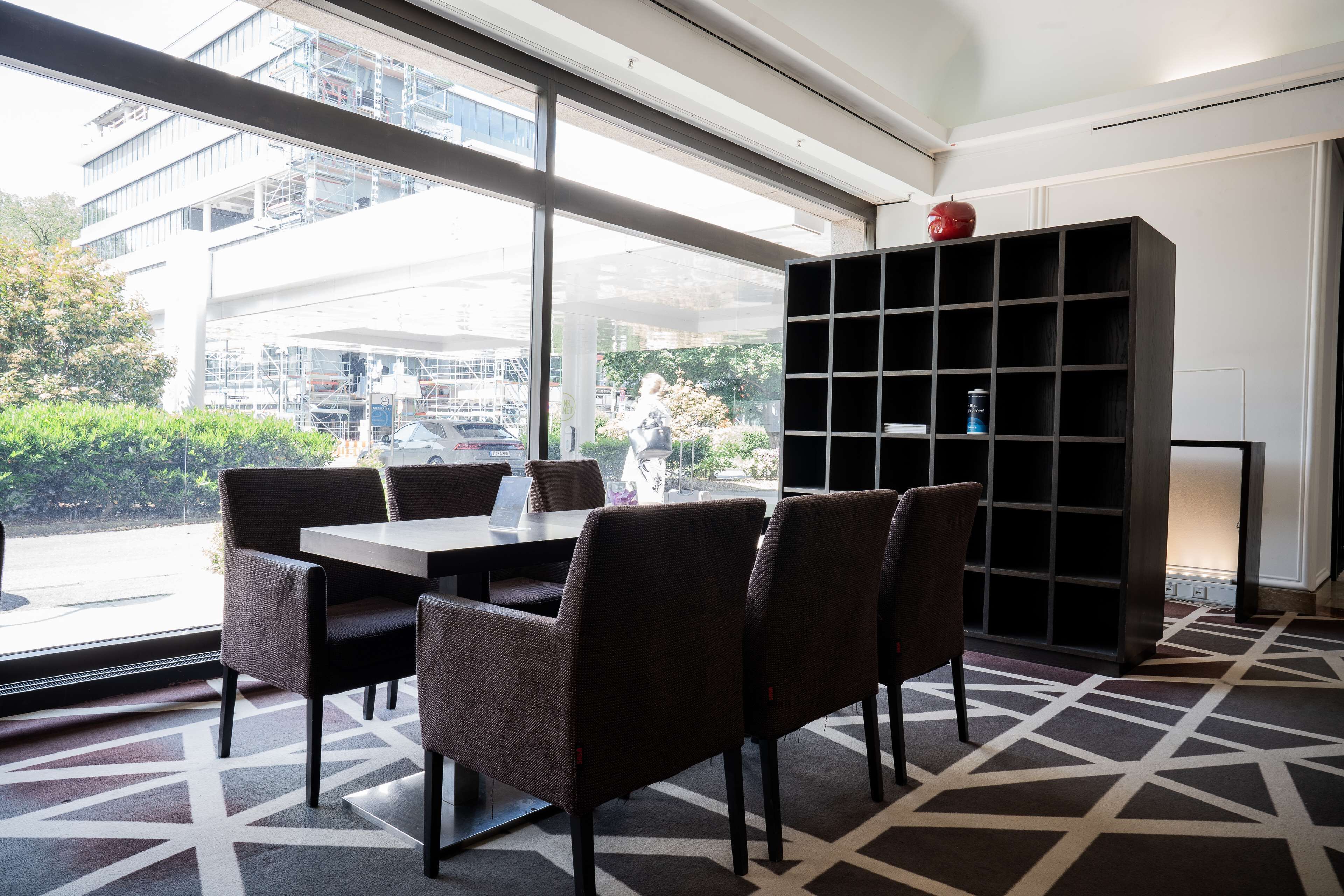 Una habitación de hotel moderna con un ventanal grande, una mesa de comedor con sillas y una estantería negra.