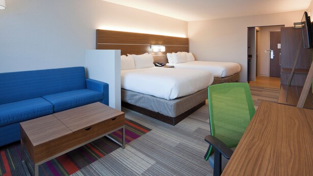 A hotel room with a blue sofa, a wooden desk, a bed with white linens, and a green office chair. - Holiday Inn Express & Suites Minneapolis – West End by IHG (Golden Valley)