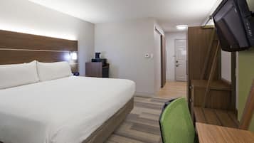 A hotel room with a large bed, a desk with a chair, a television mounted on the wall, and a wooden staircase.