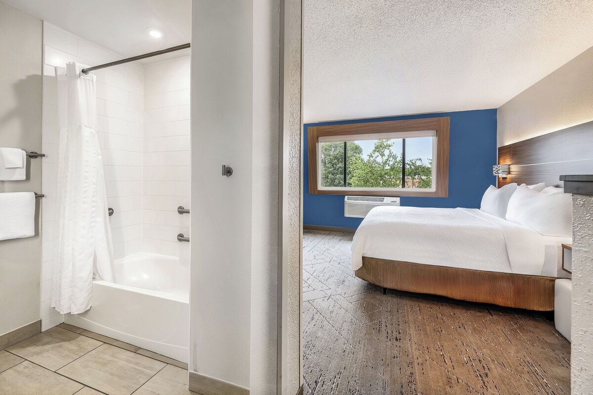 A modern bathroom with a bathtub, shower, and a large window.