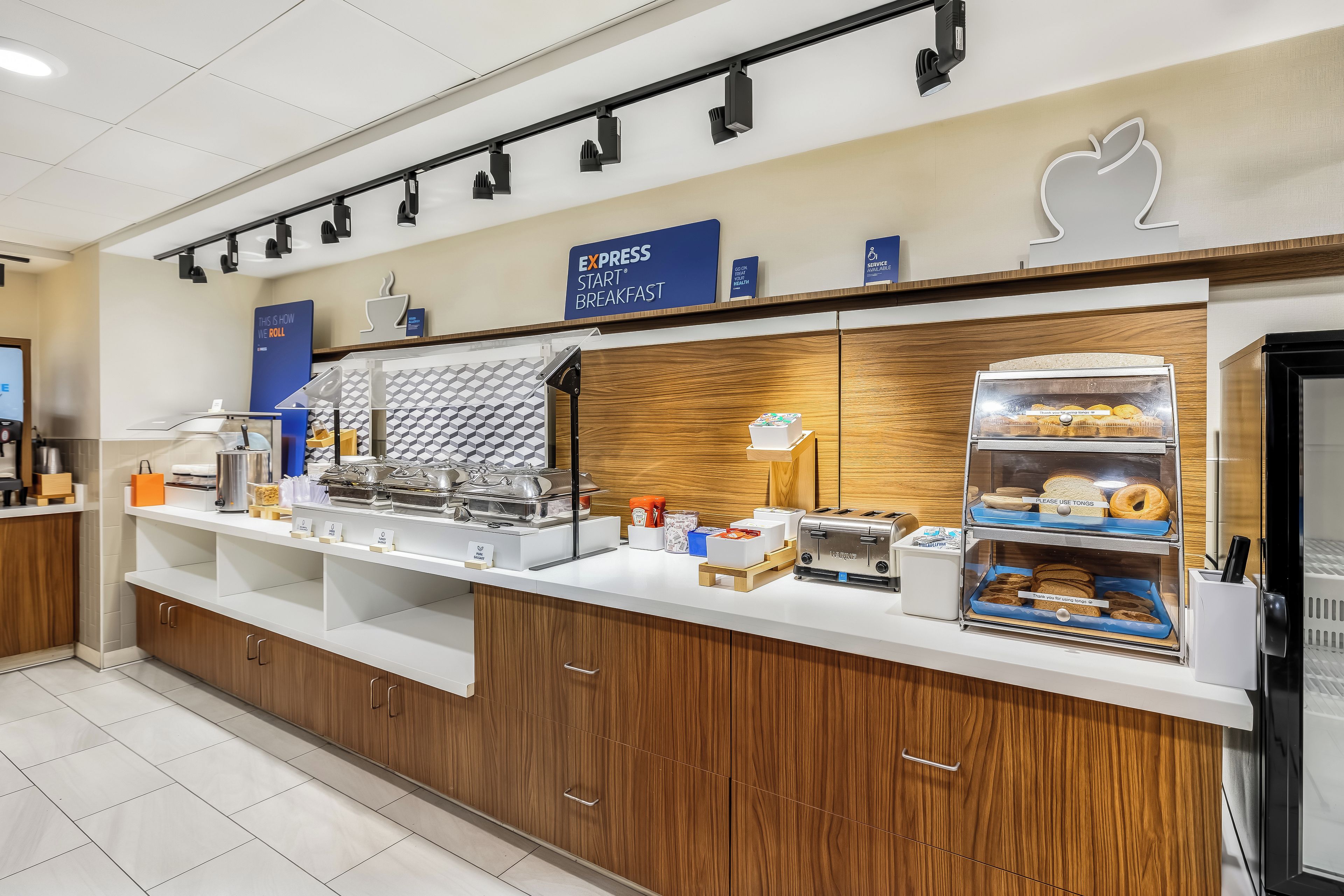 A breakfast station with a sign indicating 'Express Start Breakfast', a toaster, a refrigerator with food items, and a sign for 'Service Available'.