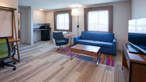 A modern hotel room with a sofa, a desk with a chair, a television, and a kitchenette. - Holiday Inn Express & Suites Minneapolis – West End by IHG (Golden Valley)