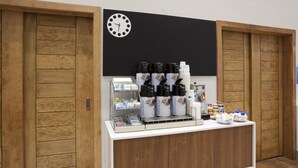 A coffee station with multiple coffee dispensers, a clock, and a counter with various items. - Holiday Inn Express & Suites Minneapolis – West End by IHG (Golden Valley)