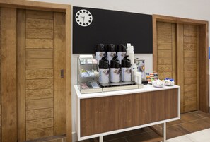 A coffee station with multiple coffee dispensers, a clock, and a counter with various items. - Holiday Inn Express & Suites Minneapolis – West End by IHG (Golden Valley)