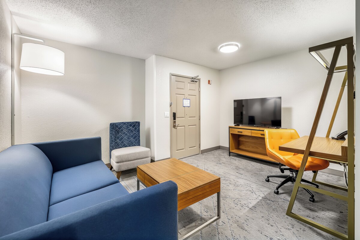 A modern hotel room with a sofa, a small table, a television, and a desk with a chair.