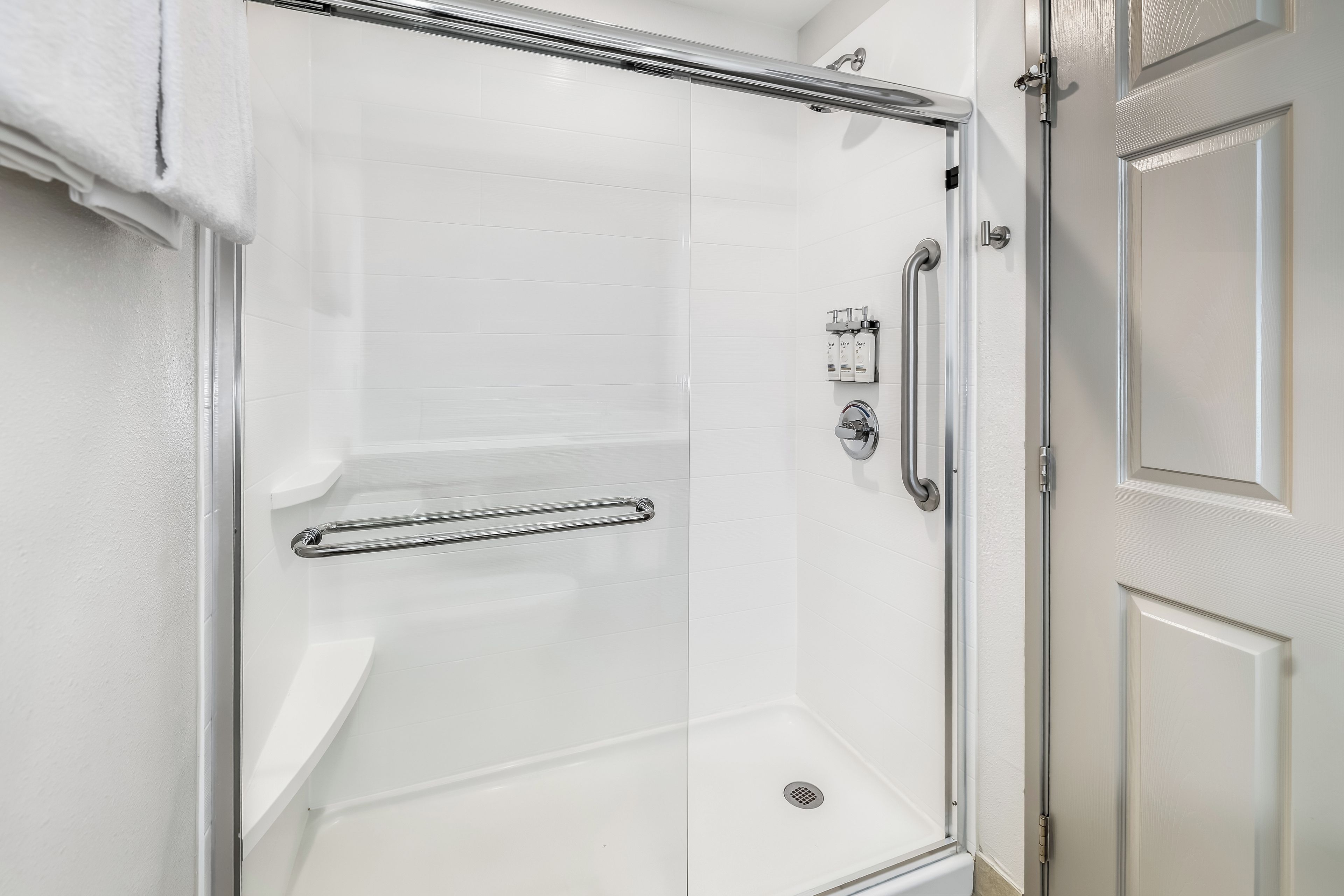 A walk-in shower with a glass door, a handrail, and a shower control panel.