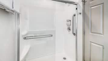 Una ducha a ras de suelo con puerta de cristal, barra de apoyo y panel de control.