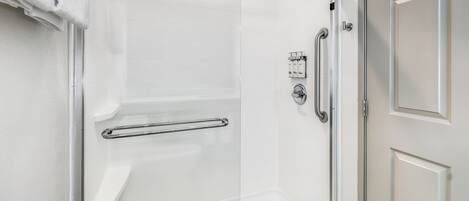 A walk-in shower with a glass door, a handrail, and a shower control panel.