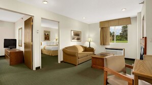 A hotel room with a bed, a sofa, a desk with a chair, a television, and a window with curtains. - Days Inn by Wyndham Rapid City (Rapid City)