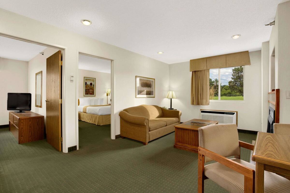 Une chambre d’hôtel comprenant un lit, un canapé, un bureau avec une chaise, une télévision et une fenêtre avec des rideaux.