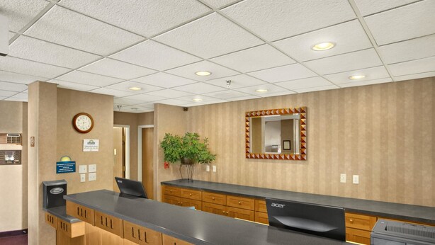 A reception desk with a clock, a plant, and a mirror. - Days Inn by Wyndham Rapid City (Rapid City)