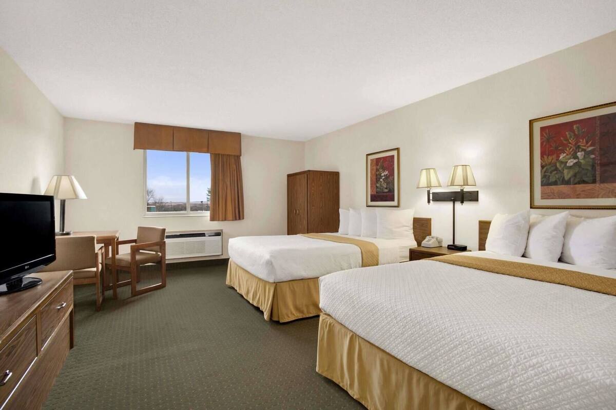 Une chambre d’hôtel avec deux lits, un bureau, une télévision et une fenêtre avec des rideaux.