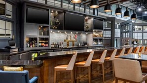 A bar area with a long counter, multiple stools, and a variety of bottles. - Wyndham Jacksonville Hotel & Conference Center (Jacksonville)