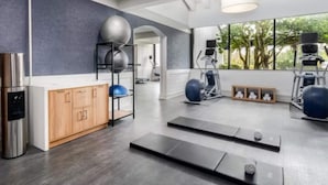 A gym with exercise equipment, a water dispenser, and a view of trees through large windows. - Wyndham Jacksonville Hotel & Conference Center (Jacksonville)