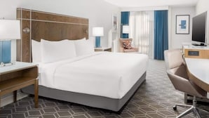 A hotel room with a large bed, a desk with a chair, a television, and a window with curtains. - Wyndham Jacksonville Hotel & Conference Center (Jacksonville)