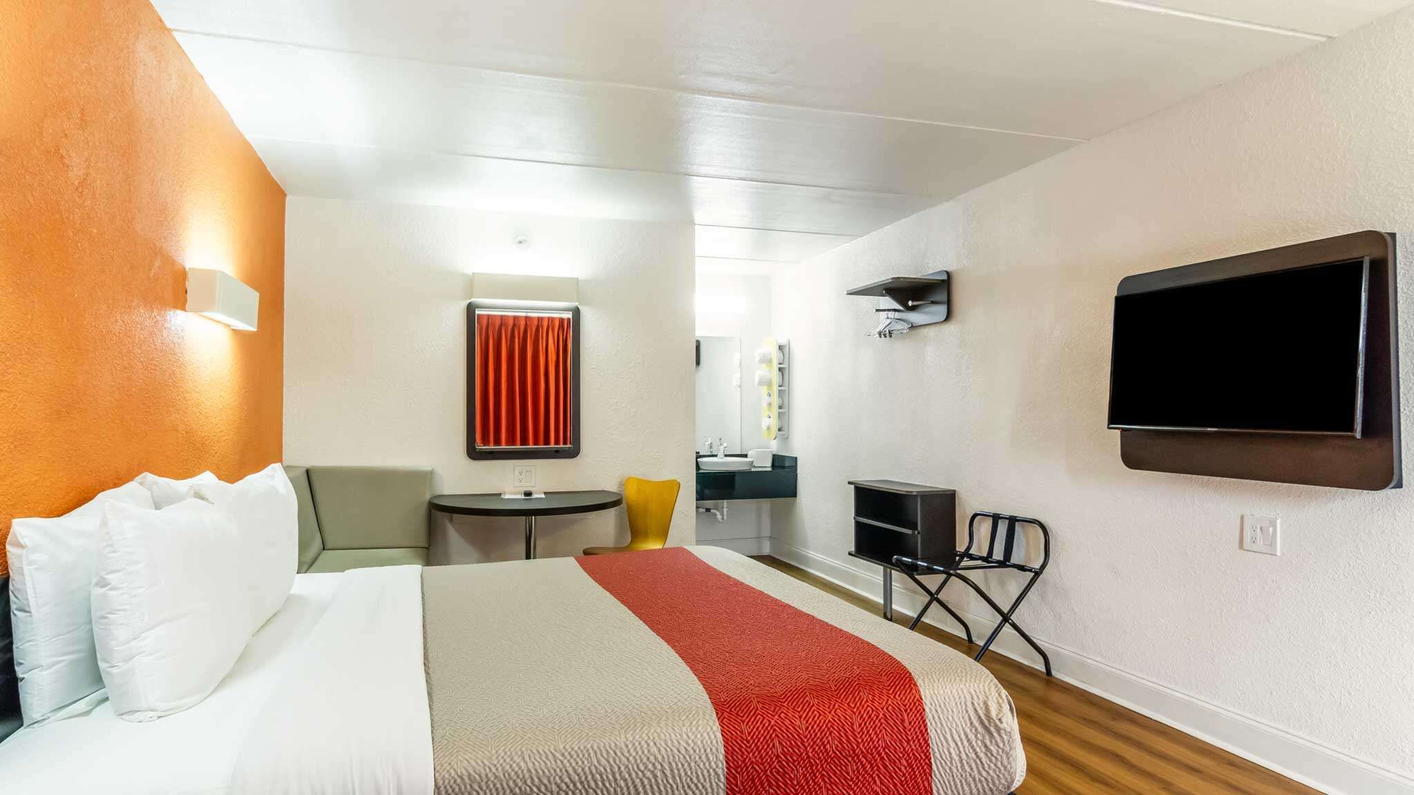Une chambre d’hôtel avec un lit, un bureau, une chaise, une télévision et une salle de bain visible à travers une porte ouverte.