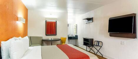 Une chambre d’hôtel avec un lit, un bureau, une chaise, une télévision et une salle de bain visible à travers une porte ouverte.