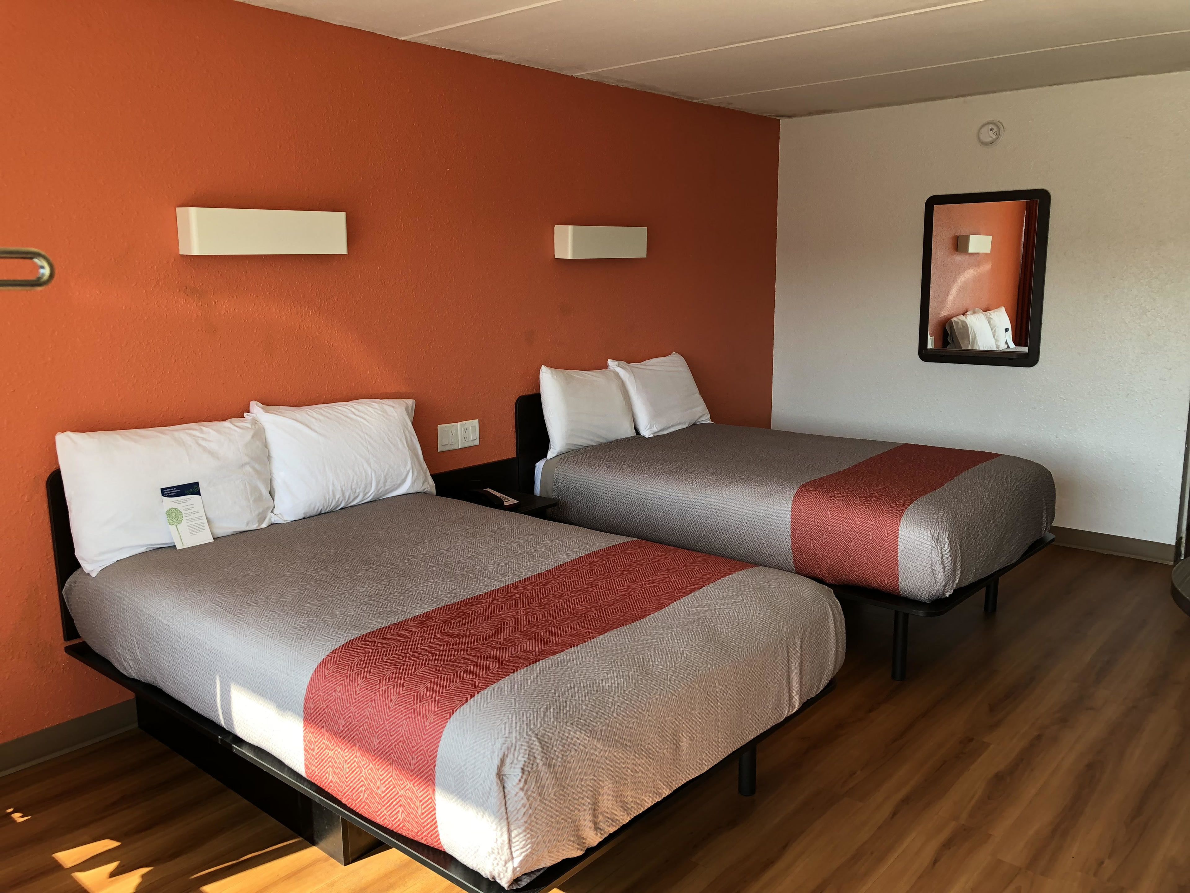 Hotelkamer met twee bedden, elk met een grijze en rode deken, witte kussens en een klein nachtkastje met een afstandsbediening.