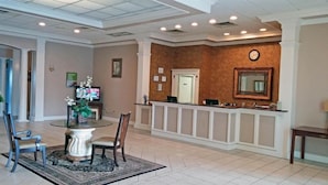 A spacious lobby with a reception desk, a dining area with a round table and chairs, and a large mirror on the wall. - Motel 6 Brunswick, GA (Brunswick)