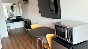 A compact kitchen with a microwave, a refrigerator, and a dining area with a table and chairs. - Motel 6 Brunswick, GA (Brunswick)