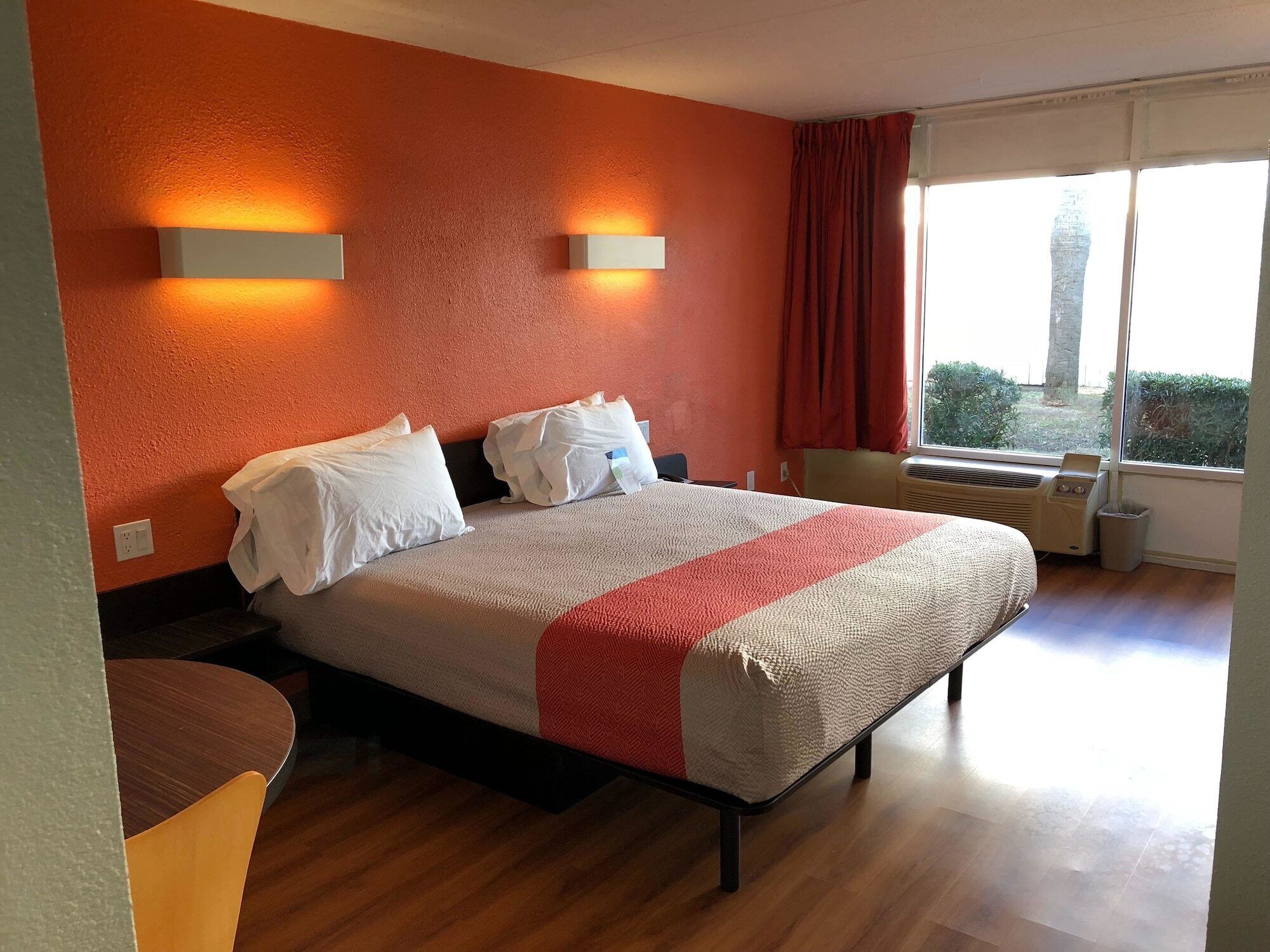 A hotel room with a bed, two wall-mounted lights, a window with curtains, and a radiator.