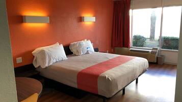 A hotel room with a bed, two wall-mounted lights, a window with curtains, and a radiator.
