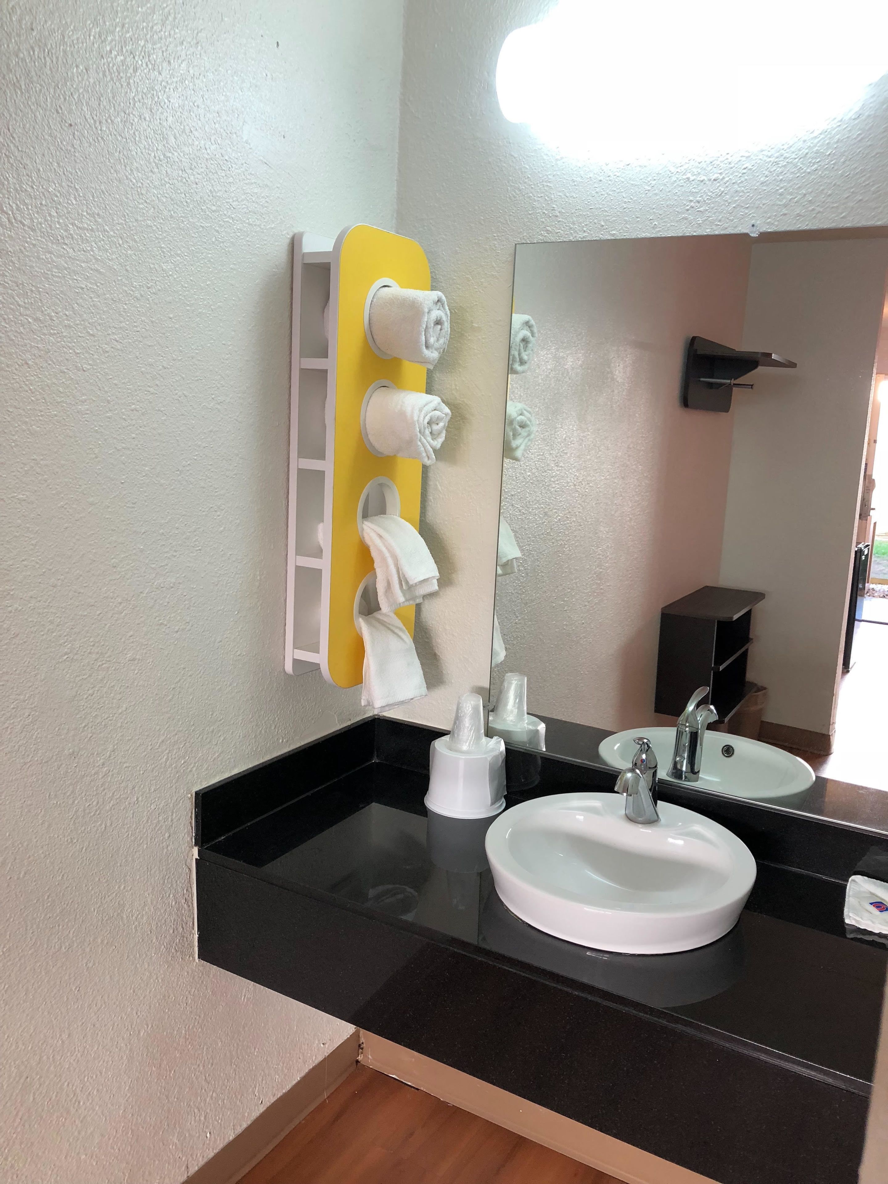 A bathroom with a black countertop, a white sink, a mirror, and a towel rack with multiple towels.
