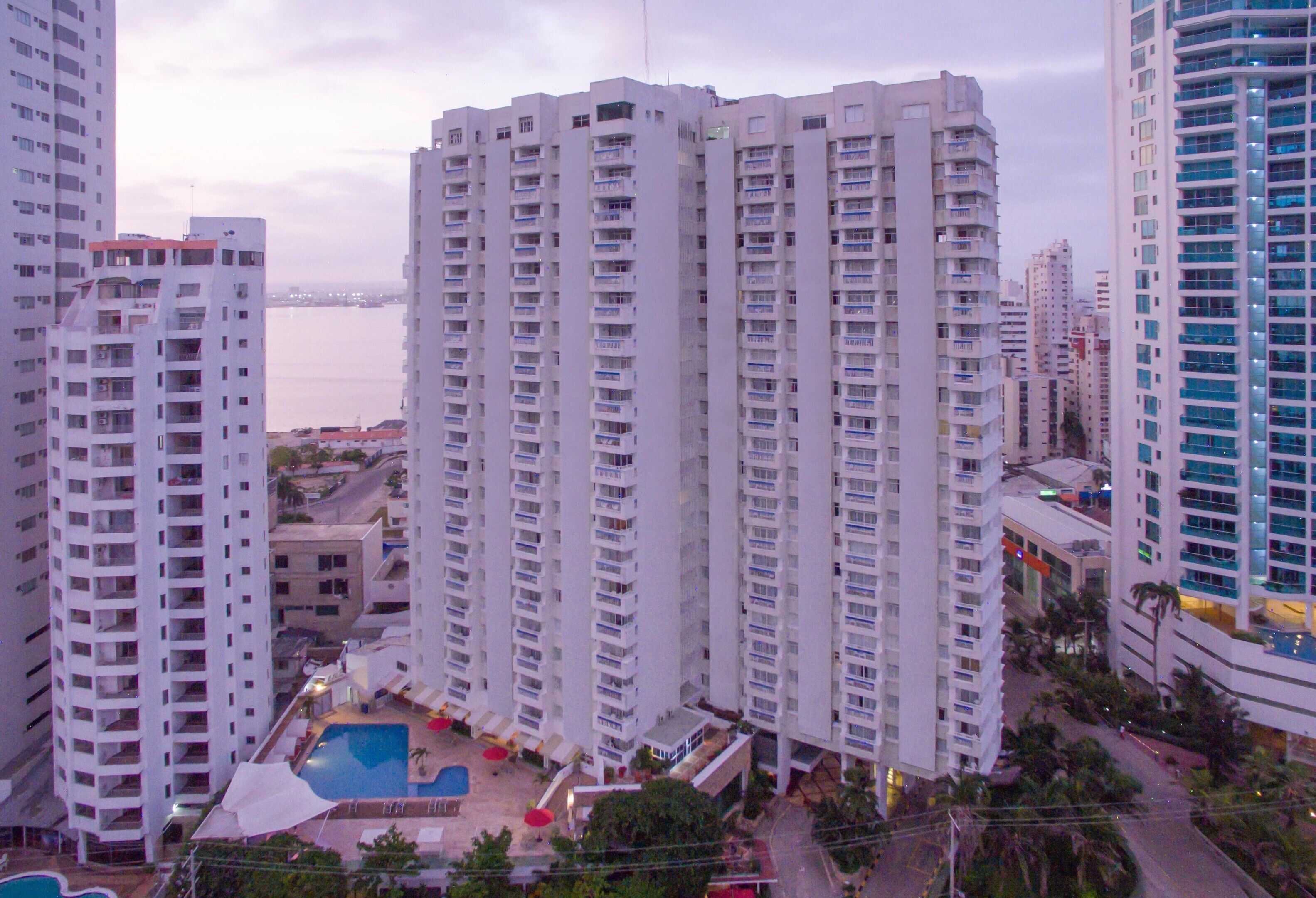 Un edificio residencial alto con varios balcones, piscina y vista a un cuerpo de agua.