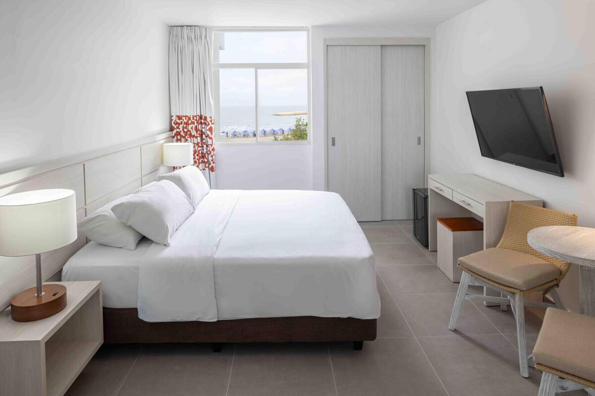 A hotel room with a bed, a desk, a chair, a TV, and a window with a view.