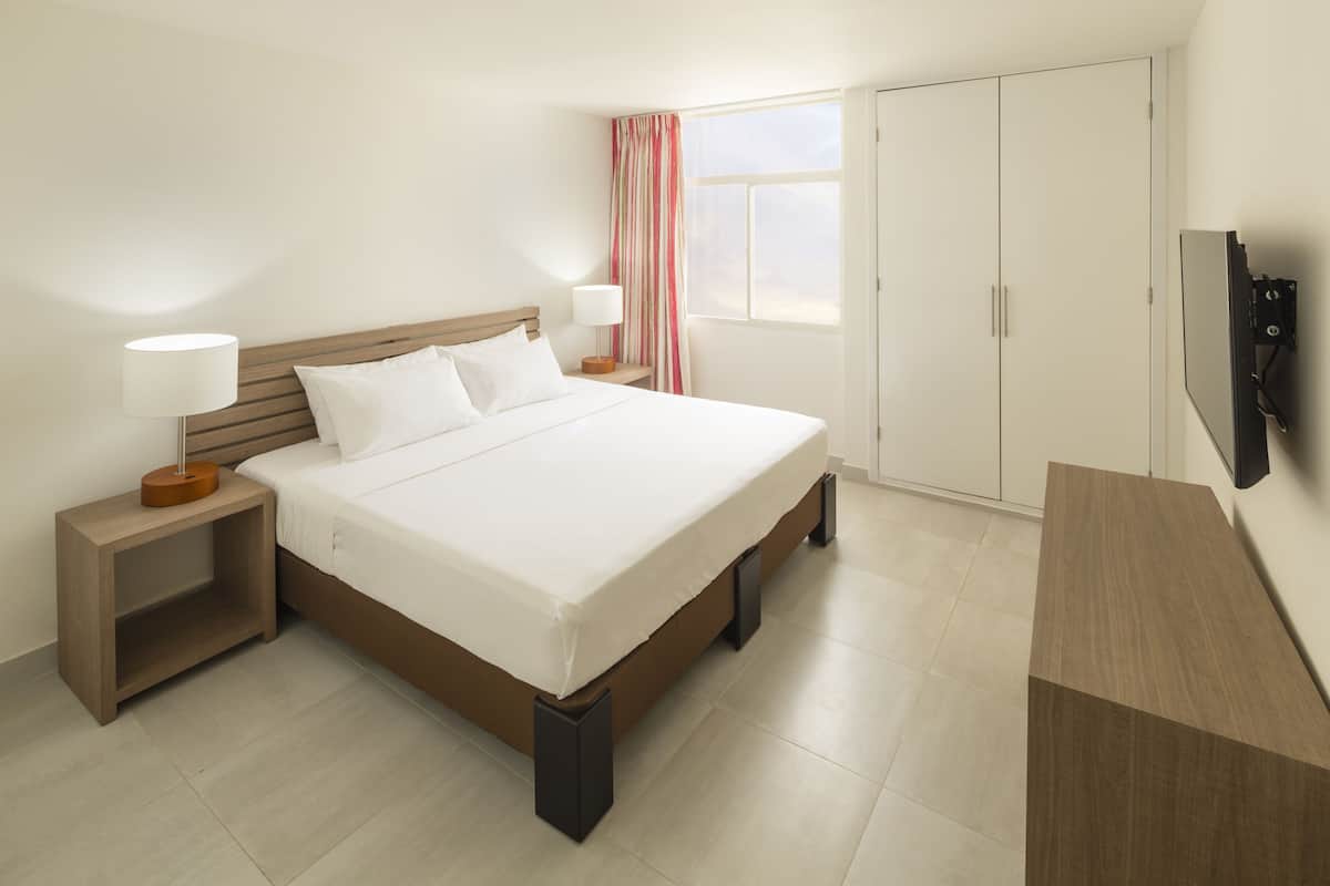 A hotel room with a large bed, bedside tables with lamps, a wardrobe, and a TV mounted on the wall.