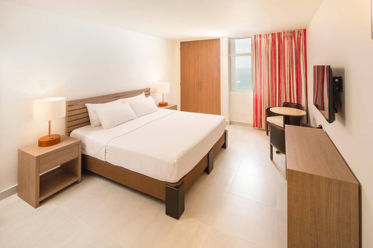 A modern hotel room with a large bed, bedside tables, a desk, and a TV.